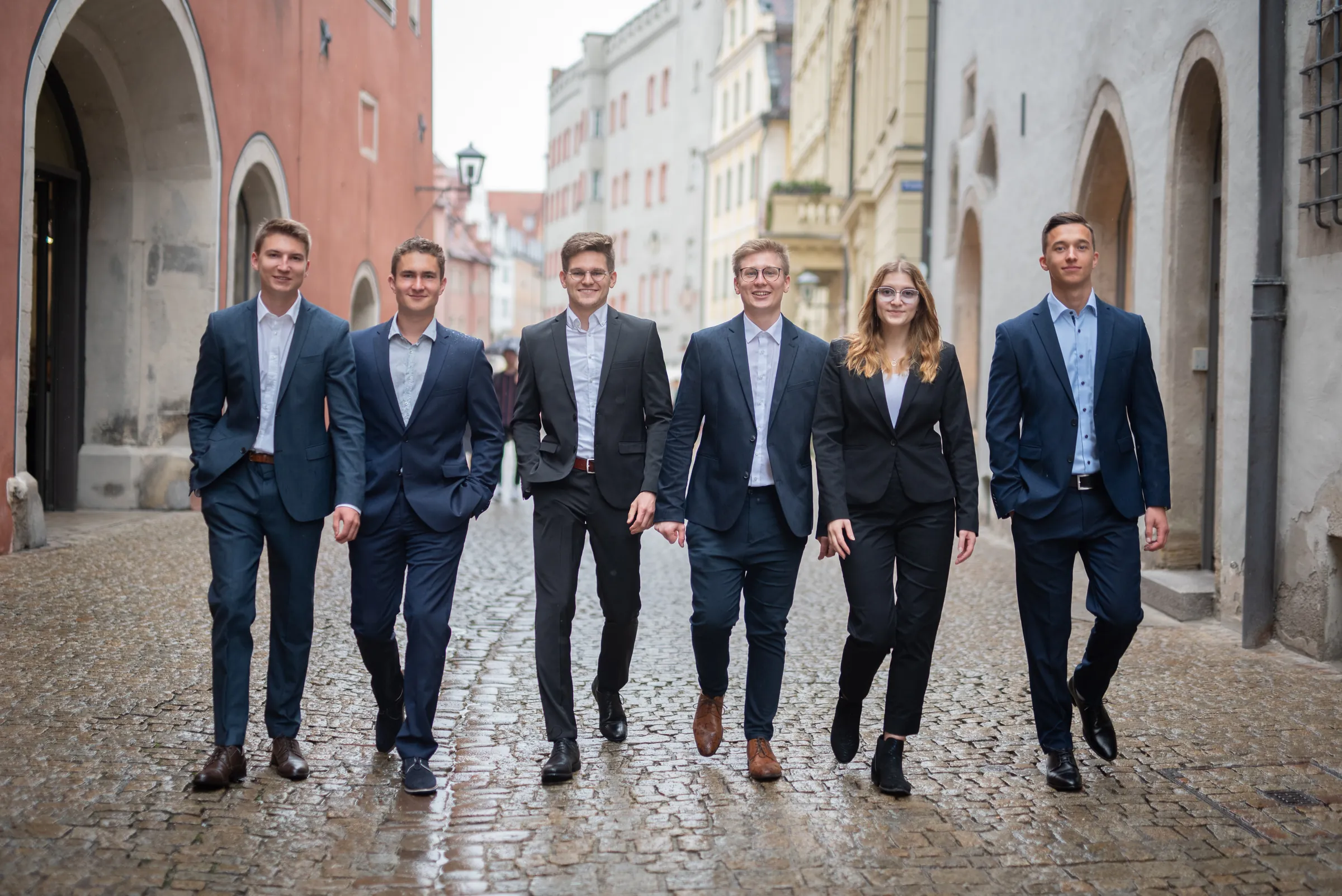 Gruppenfoto des Vorstands 2022–2023: sechs Personen in Business-Kleidung gehen nebeneinander über eine regennasse Kopfsteinpflastergasse in der Altstadt.